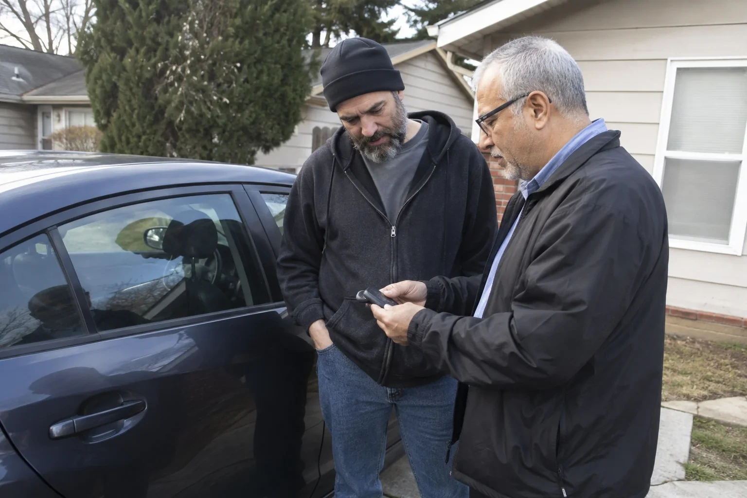 Two adults discussing a key fob beside a parked car.
